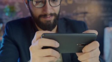 Geceleri akıllı telefon kullanarak oyun oynayan mutlu Ortadoğu çalışanlarının yakın plan görüntüleri.