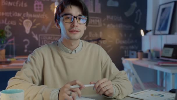 Retrato em câmera lenta de um jovem hipster sentado em um escritório criativo escuro — Vídeo de Stock