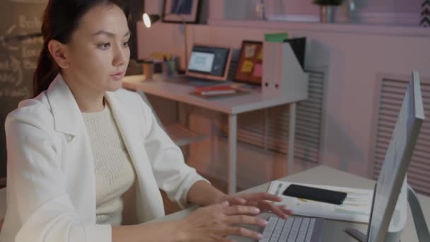 Mujer de negocios joven cansado trabajando con pc mecanografía luego estirando los brazos y el cuello en la oficina oscura — Vídeos de Stock