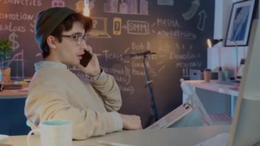 Arkadaş canlısı bir çalışan cep telefonuyla müşteriyle konuşuyor. Yaratıcı ofiste geç saatlere kadar çalışan belgeleri kontrol ediyor.