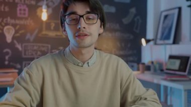 Yaratıcı genç çalışan, karanlık ofiste yabancı ortaklarla sanal görüşme yaparken konuşuyor.