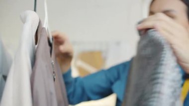Asyalı kadın terzinin portresi modern galeride elbise askılarını kontrol ediyor.