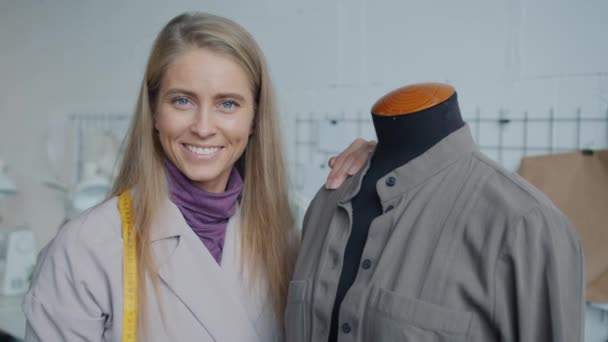 Портрет успешного портного, стоящего в студии рядом с манекеном с новой современной одеждой — стоковое видео