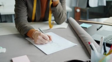 Stüdyoda tasarımcı olarak çalışırken erkek ellerinin yeni moda giysiler çizdiği yakın plan çekimler.
