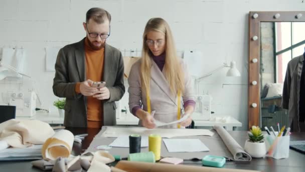 Lány és fiú kreatív tervezők dolgoznak stúdió ellenőrzése vázlatok és okostelefon használata — Stock videók