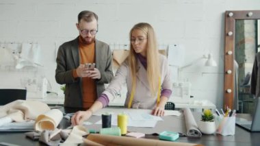 Kıyafet tasarımcıları çizimlere bakıyor kumaşı seçiyor ve kapalı alanda akıllı telefon kullanıyor.