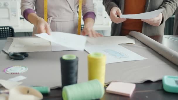 Руки творческих людей, работающих в студии дизайна одежды, держат эскизы в поисках идей — стоковое видео