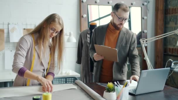 Mannen en vrouwen collega 's kleermakers kiezen materiaal voor nieuw kledingstuk werken samen met behulp van laptop — Stockvideo