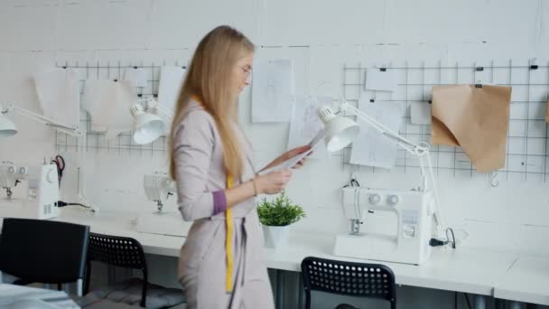 Pensieve jonge dame naaister opknoping tekeningen van kleding aan boord in de werkplaats — Stockvideo