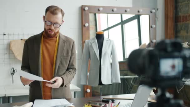 Mężczyzna projektant mody nagrywanie wideo dla internet blog pokazując szkice mówienie i gestykulacji pracy w studio — Wideo stockowe
