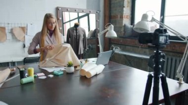 Profesyonel kıyafet tasarımcısı stüdyoda kamera kullanarak terzilik hakkında konuşuyor.
