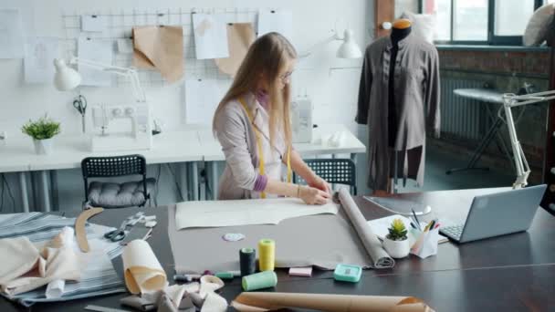 Konstruktør syr nytt klesplagg med tegning av materiale som arbeider alene i det moderne studioet – stockvideo