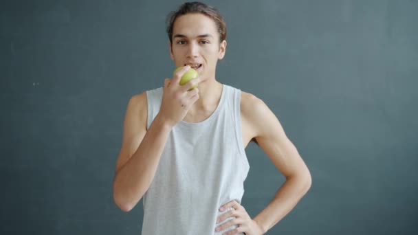 Retrato de câmera lenta de mestiço comendo maçã e sorrindo no fundo de cor cinza — Vídeo de Stock