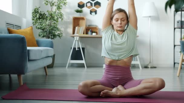Porträtt av attraktiv dam som gör yoga stretching i lotusposition träning på matta i lägenhet — Stockvideo