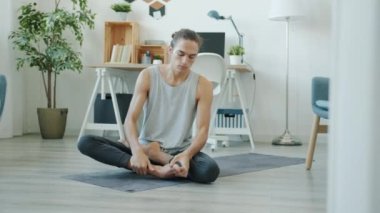 Genç sporcu evde tek başına yoga minderinin üzerinde oturarak denge kuruyor..