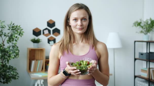 Портрет симпатичной блондинки, держащей миску салата в помещении в квартире — стоковое видео