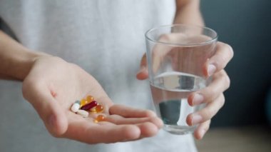 Evde erkek eli vitamin hapları ve bir bardak su tutarken yakın plan.