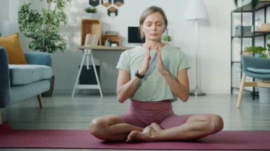 Spor kıyafetli rahat bir kız Lotus pozisyonunda meditasyon yapıyor Yoga minderinin üzerinde gözleri kapalı oturuyor namaste.