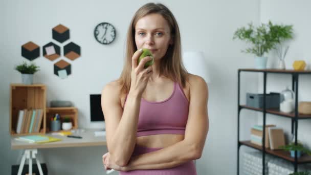 スローモーションポートレートの陽気なスポーツ女性食べるリンゴと笑顔見てカメラで家 — ストック動画