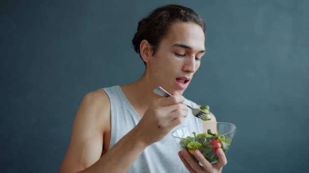 Portret młodego tysiąclecia jedzącego sałatkę warzywną cieszącego się zdrową żywnością na szarym tle — Wideo stockowe
