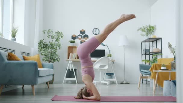 Vista lateral de chica atractiva haciendo cabecera concentrada en la actividad de yoga en apartamento — Vídeos de Stock