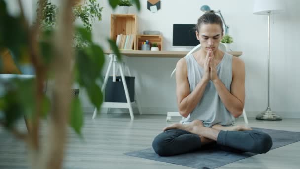 Powolny ruch mieszanej rasy człowiek medytujący w domu poruszając rękami namaste siedzi na macie do jogi w nowoczesnym mieszkaniu — Wideo stockowe