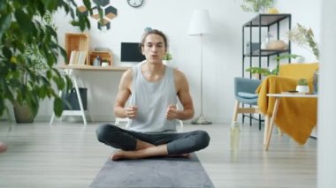 Spor vlogcusu portresi yoga dersleri veriyor ve apartmandaki kameraya bakarak egzersiz yapıyor.