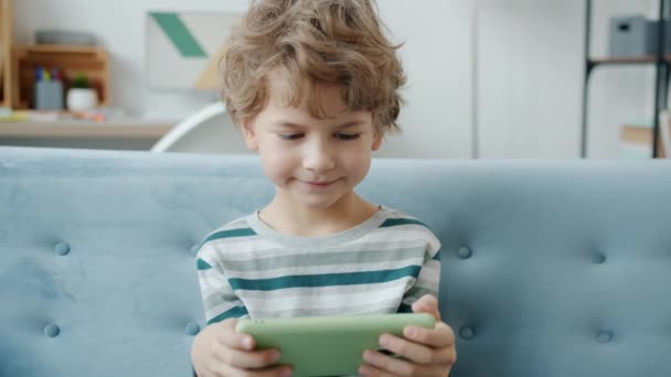 Медленное движение радостного ребенка, веселящегося с видеоигрой на смартфоне, играющего в одиночестве дома — стоковое видео