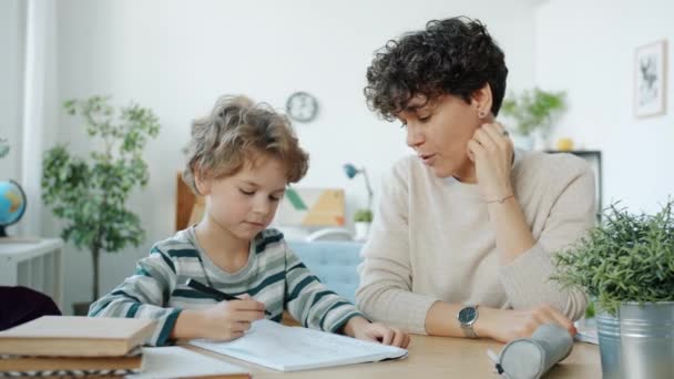 Malý chlapec dělá domácí úkol s matkou mluví psaní směje se u stolu v bytě — Stock video