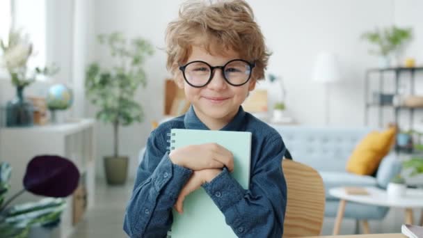 Портрет повільного руху розумного маленького хлопчика генія в окулярах, що тримає книгу вдома — стокове відео