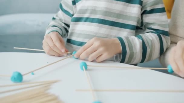 Detailní záběr rukou dospělý a dítě dělá řemeslo s dřevěnými tyčinkami a hrát těsto doma — Stock video