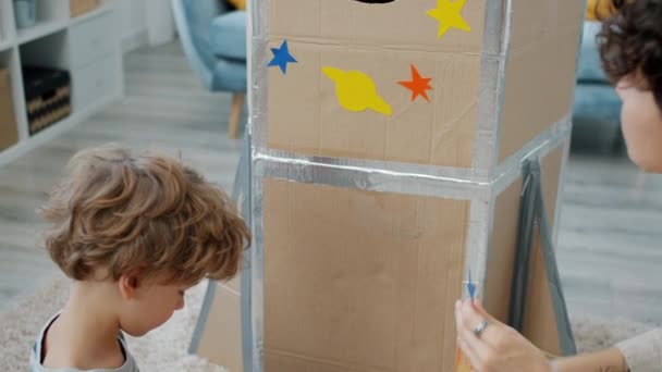 Femeie tânără și fiu mic decorarea rachetei handmade cu autocolante de design spațial la domiciliu — Videoclip de stoc