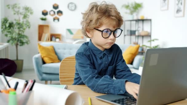 深刻な子供で眼鏡作業でラップトップコンピュータで座って机に家 — ストック動画