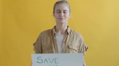 Sarı arka planda Save Planet tabelası tutan sarışın kızın yavaş hareketi