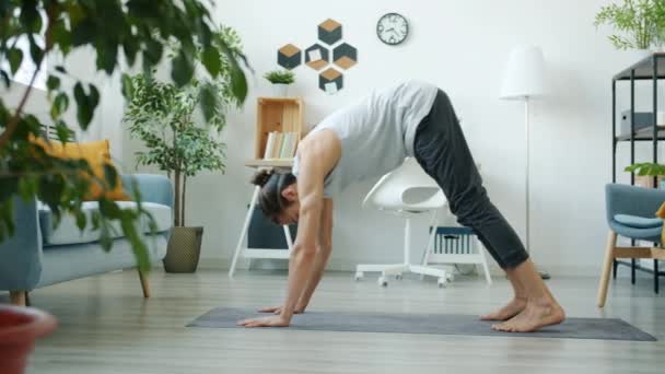 Vista lateral de un joven atleta haciendo ejercicios de yoga en casa disfrutando de la práctica doméstica solo — Vídeo de stock