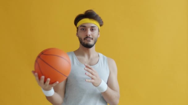 Portrait of joyful Indian guy having fun with basketball playing alone on yellow background — Stock Video