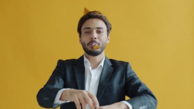 Orta Doğulu, parti şapkası takmış, doğum gününü kutlayan, düdük çalan bir adamın ağır çekim portresi.