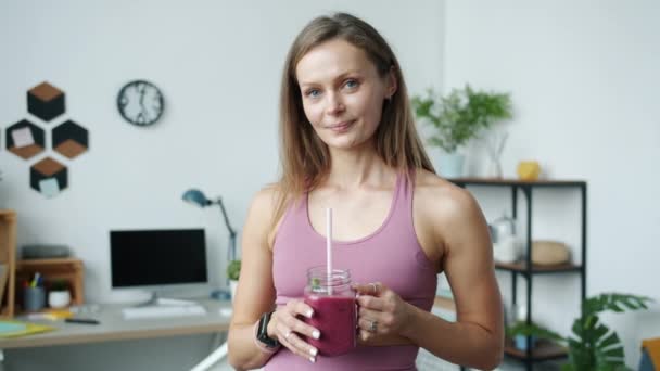 Slow motion porträtt av söta idrottskvinna som håller smoothie och ler stående hemma — Stockvideo