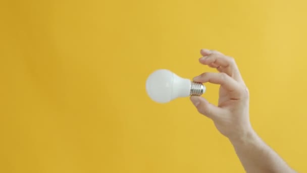 Movimento lento da mão masculina levantando lâmpada de baixa energia no fundo amarelo — Vídeo de Stock