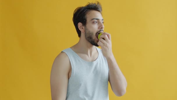 Portrait d'un bel homme arabe mangeant des pommes et souriant sur fond jaune — Video