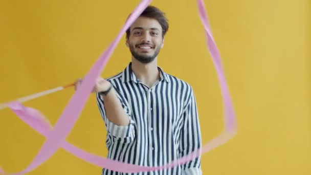 Homme arabe ludique dansant et agitant ruban de gymnastique artistique sur fond jaune — Video