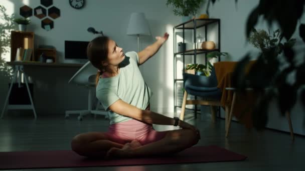 Медленное движение красивой девушки, делающей упражнения на растяжку сидя в позе лотоса дома — стоковое видео