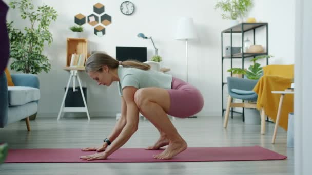 Sidovy av stark ung kvinna som gör yoga balansering på armarna motionerar hemma — Stockvideo