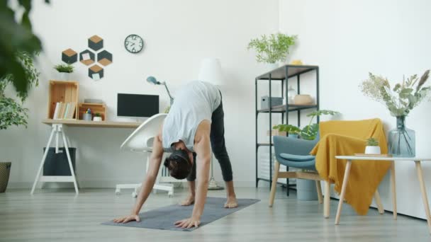 Yakışıklı genç adam evde yoga yapıyor. Vücudunu paspasa geriyor. — Stok video