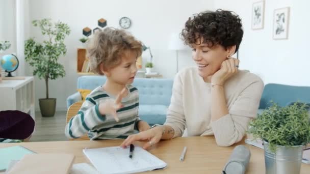 Jongen doet huiswerk met mama knuffelen praten doen high-five binnen thuis — Stockvideo