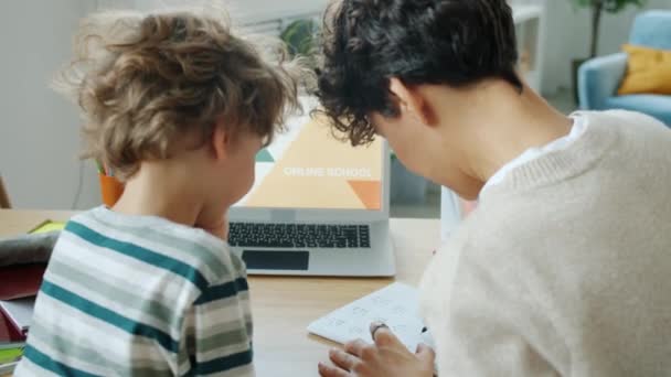 Mère aider les enfants intelligents à étudier l'écriture et à regarder un ordinateur portable avec le contenu de l'école en ligne dans l'appartement — Video