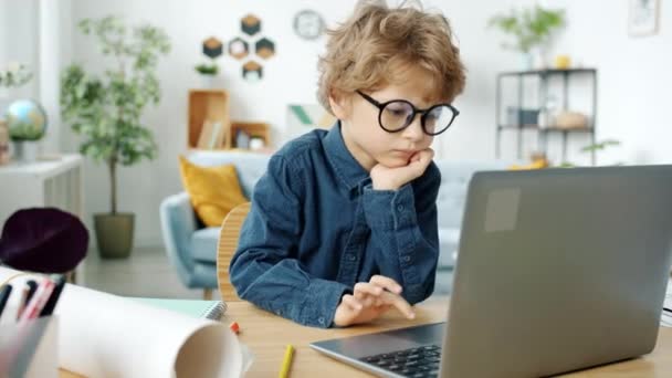 アパートの活動に集中したノートパソコンのタイピングを使用して眼鏡をかけて深刻な子供 — ストック動画