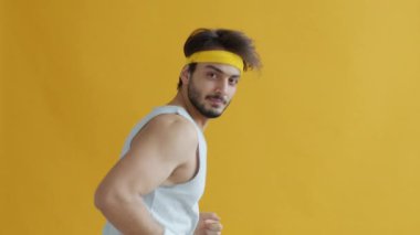 Yakışıklı Arap koşucunun portresi koşuyor ve sarı arka planda kameraya bakıyor.