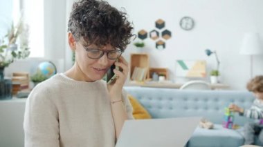 Anne cep telefonuyla konuşuyor, çocuk oynarken evde çalışıyor.