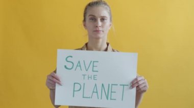 Sarı zemin üzerinde Save Planet pankartı tutan ciddi kadın aktivistin portresi